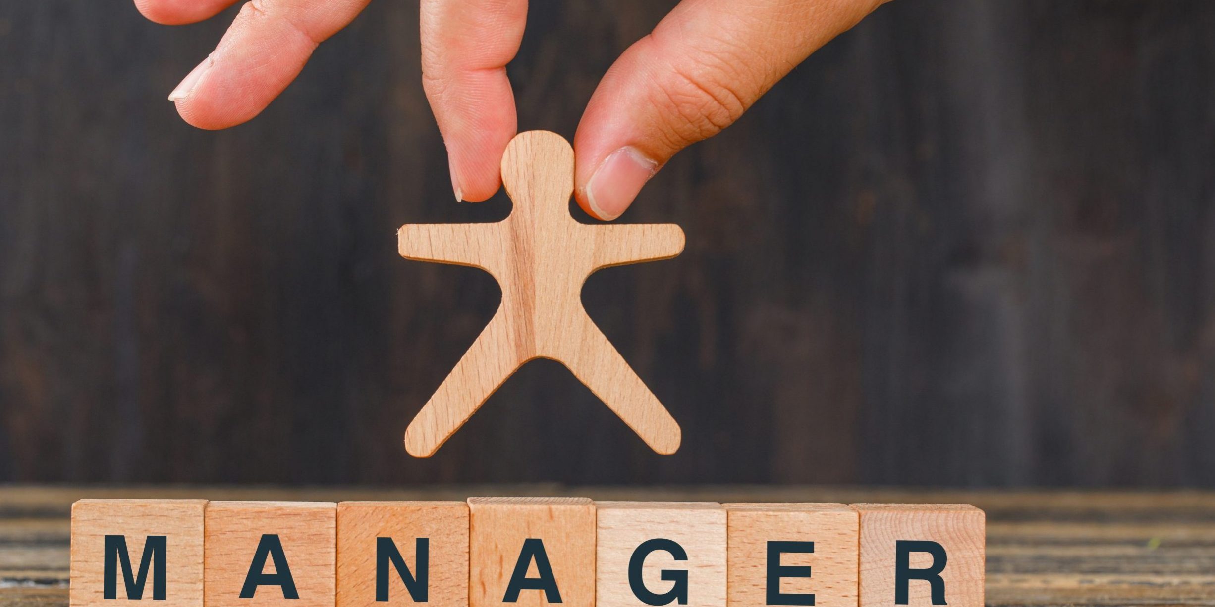 Management concept with wooden cubes on wooden background side view. hand holding human model. Difficultés du Management de proximité