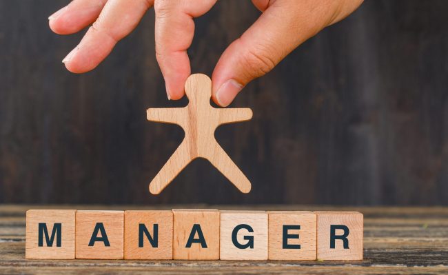 Management concept with wooden cubes on wooden background side view. hand holding human model. Difficultés du Management de proximité